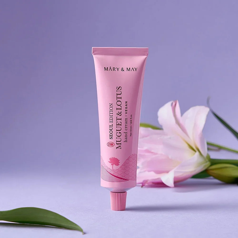 Mary&May Muguet & Lotus Hand Cream 50 ml de pie con una flor al fondo